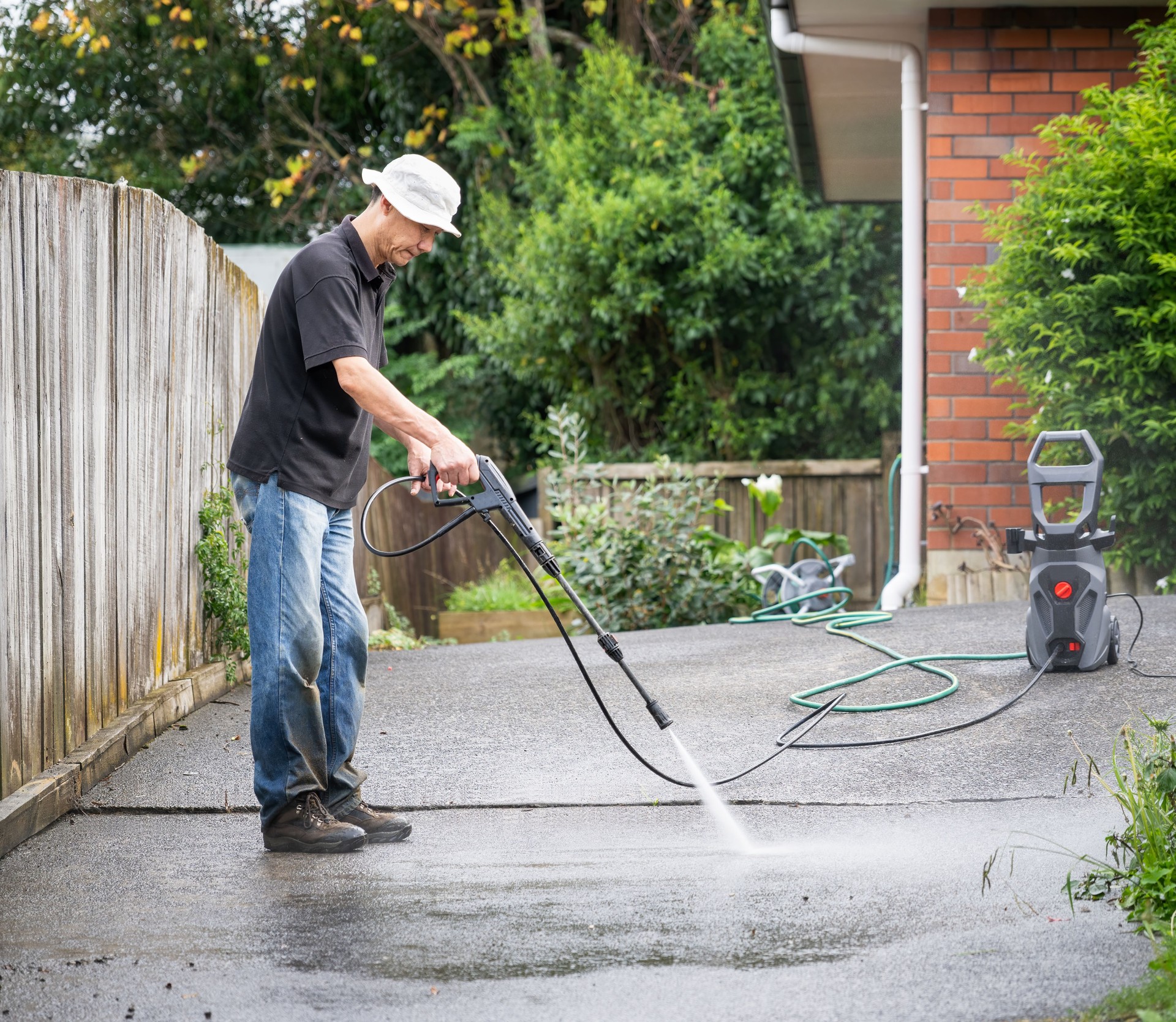 Man cleaning concrete driveway using a pressure washer.